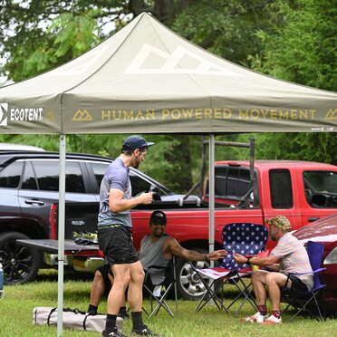 A group of men relaxing after a race under a green, printed Ecotent canopy tent.